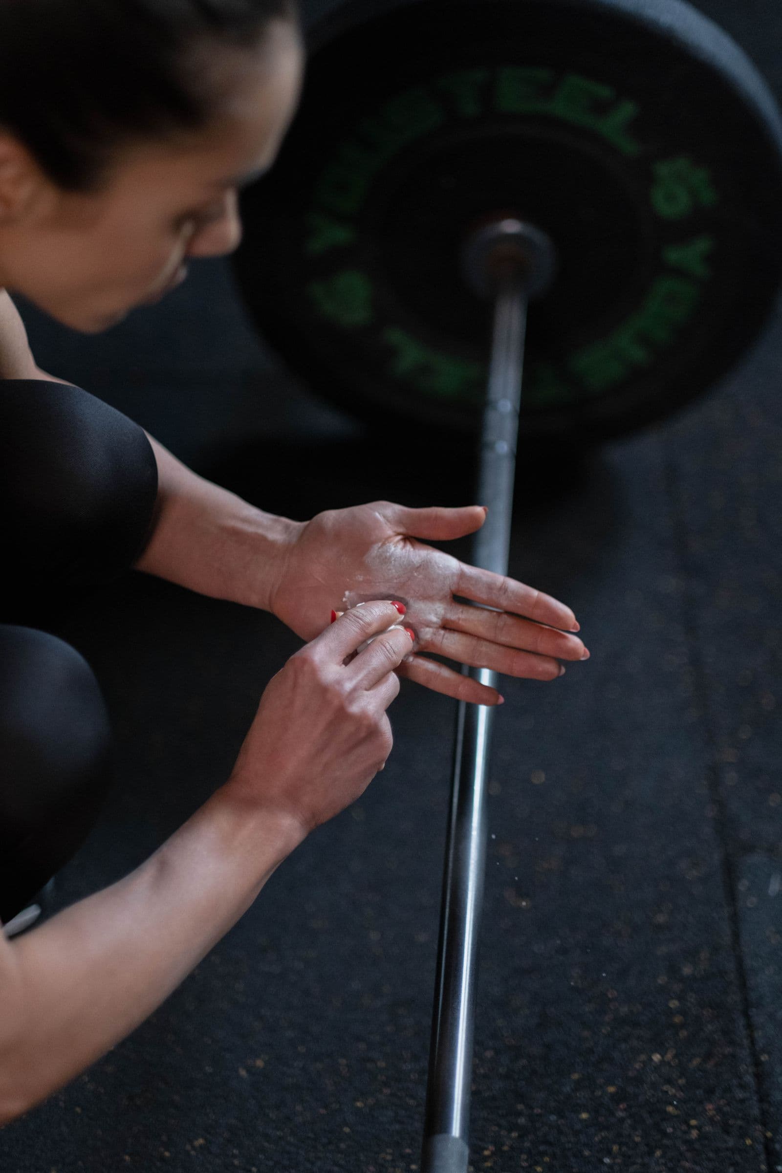 An athlete chalking her hands beside a loaded barbell
